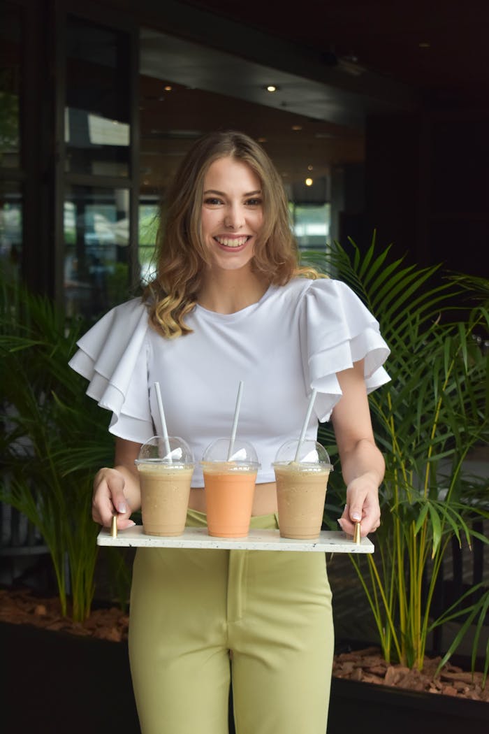 Caucasian woman with a smile, holding a tray with four drinks in an indoor setting.